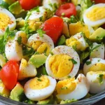 Bowl of egg salad with cherry tomatoes, avocado, and herbs.